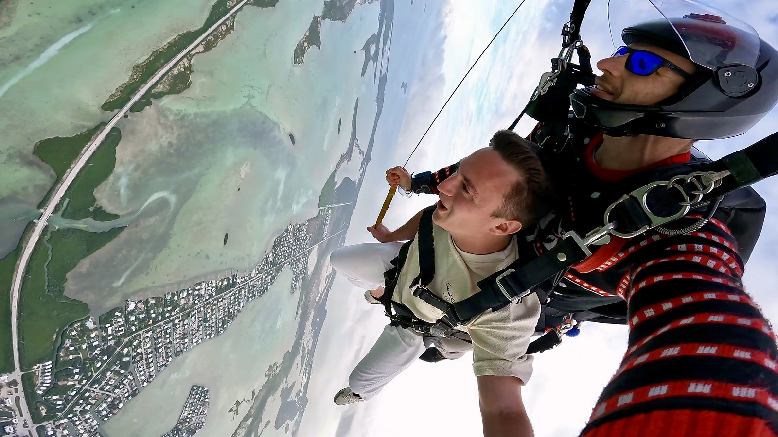 Uranik under the canopy on a tandem skydive above a turquoise coastline.