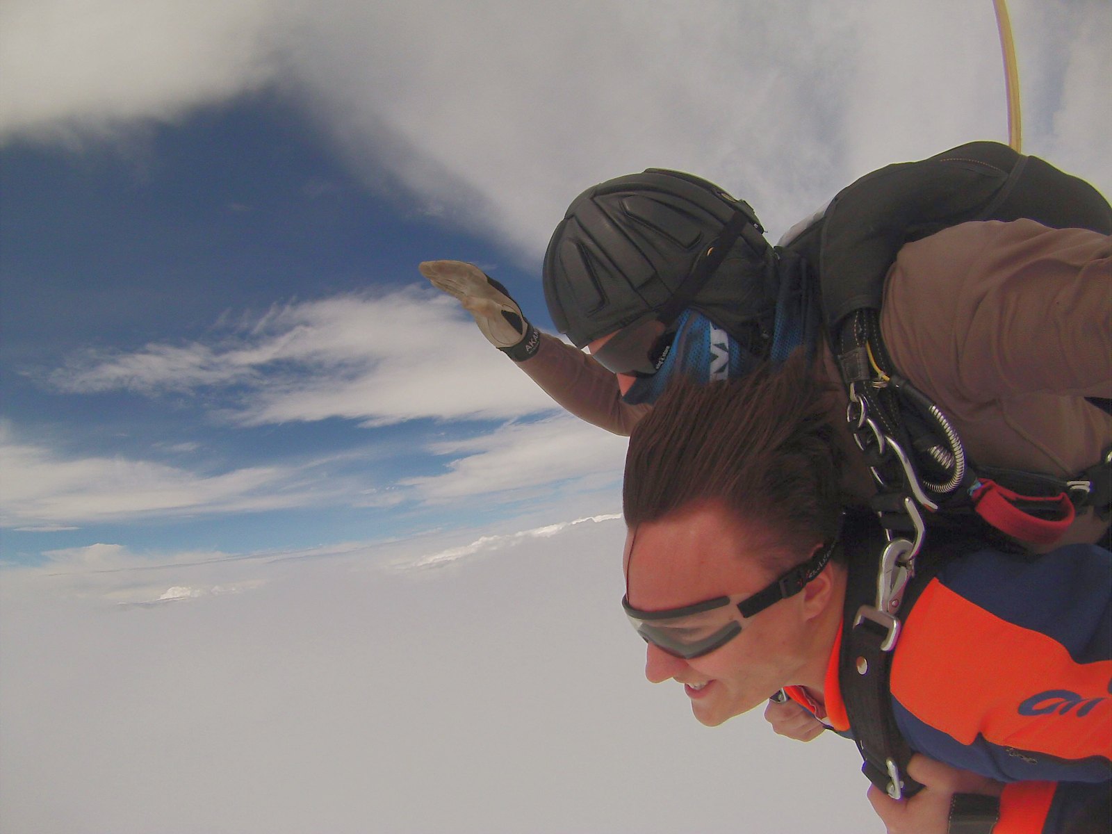 Uranik in an orange jumpsuit during tandem freefall above the clouds.